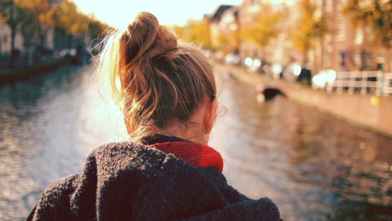 the back of a teenager's head as they face a sunlit river with their hair in a messy bun