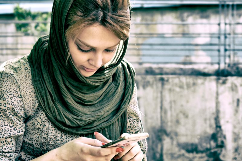 a young person in a headscarf looks at their phone