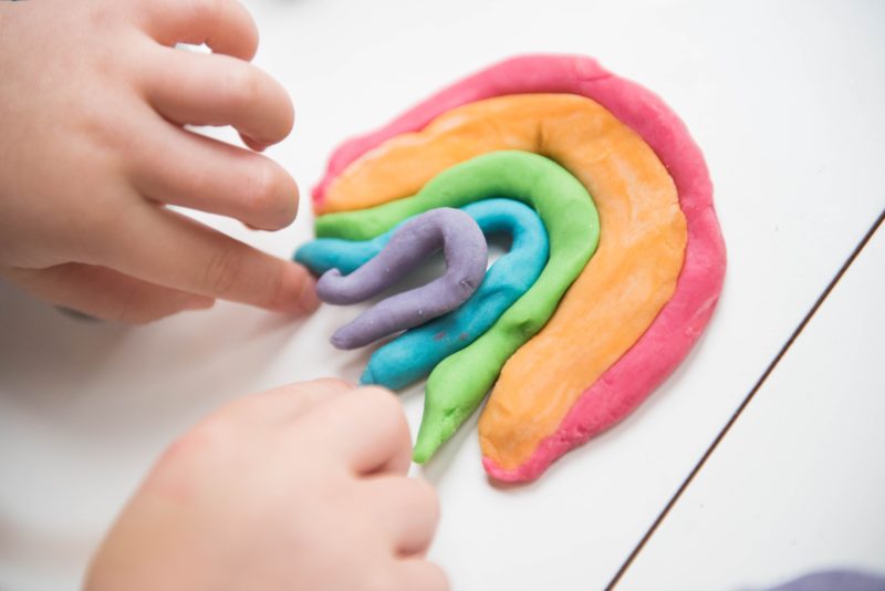 a child's hands making a rainbow out of coloured playdough