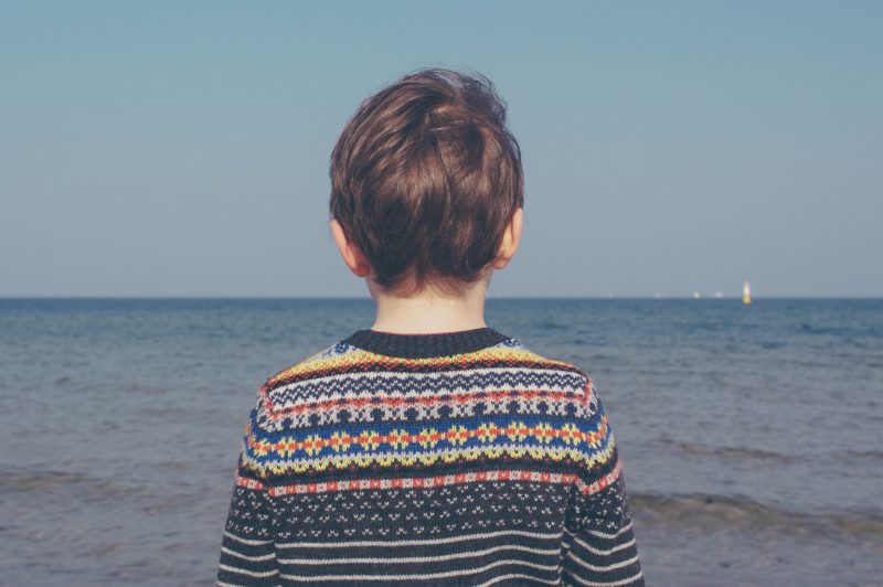 autism assessment: a young child looking at the sea, wearing a stripey jumper