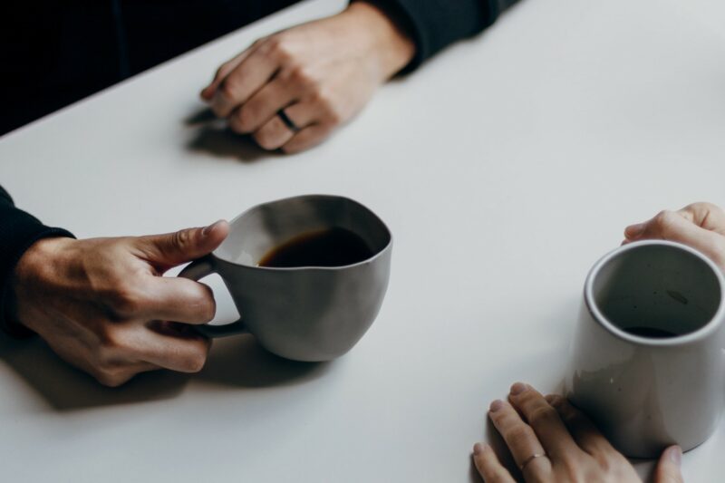 Two pairs of hands holding coffee cups on a table opposite eachother.