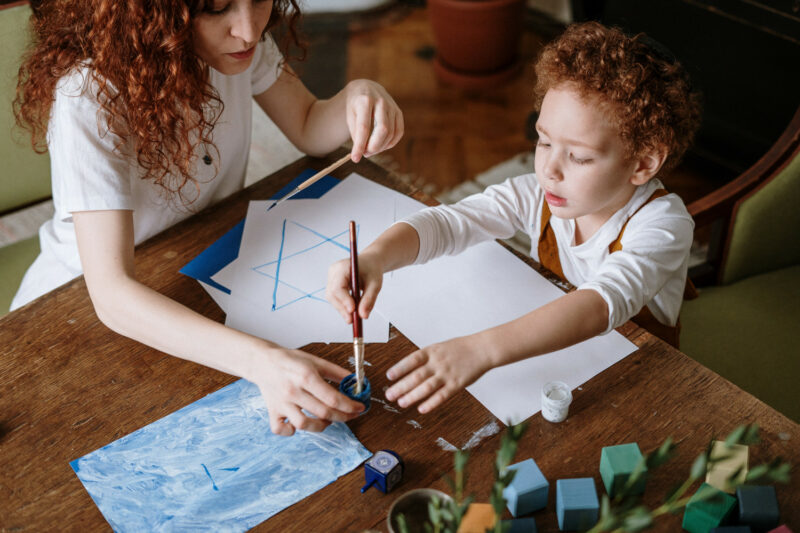 A woman helping a young child with a painting activity.