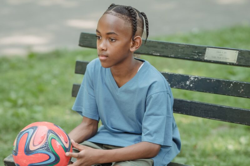 Boy sitting on a bench holding a football.