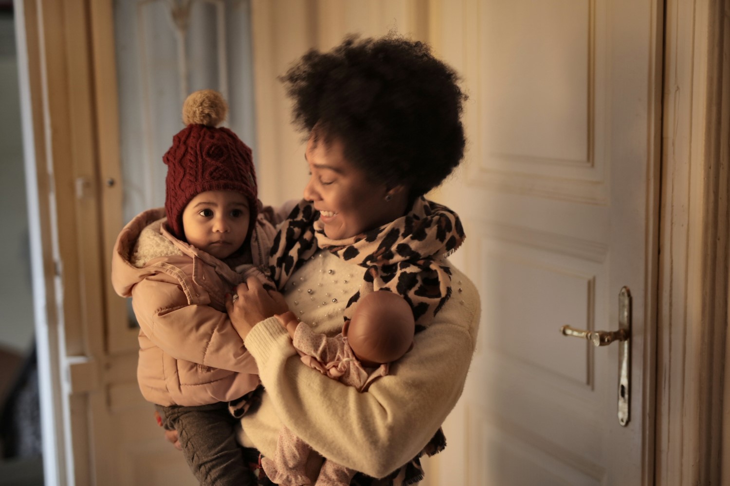 A woman holding a small child who is wearing a coat and bobble hat.